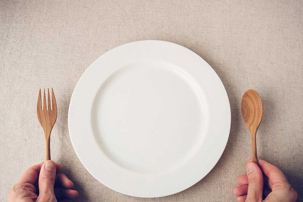 An empty plate and person's hands holding a wooden fork and spoon